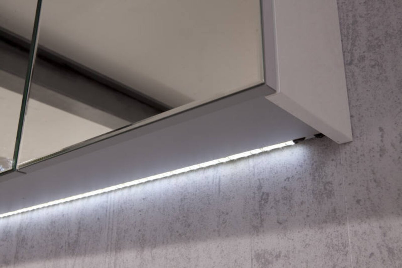 Puris LED-Waschtischbeleuchtung SPEED LED-Waschtischbeleuchtung von unten betrachtet, montiert an einem Spiegel mit Betonwand im Hintergrund.