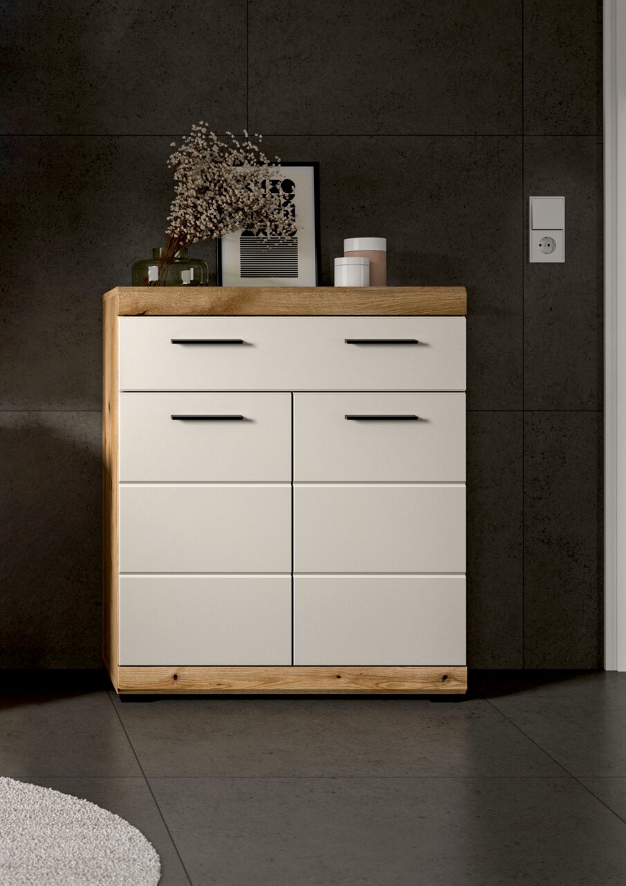 Moderne Kommode in Weiß mit Holzrahmen und schwarzen Griffen, frontal aus Augenhöhe vor dunkler Wand, dekoriert mit Vase, Bild und Dosen auf der Ablage.