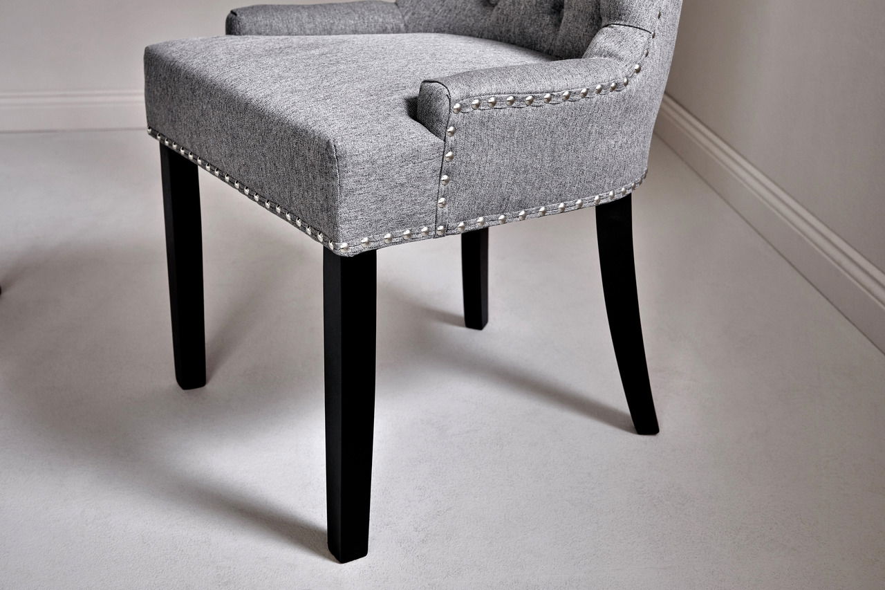 Grauer Polsterstuhl mit Nietenverzierung und schwarzen Beinen, seitliche Perspektive