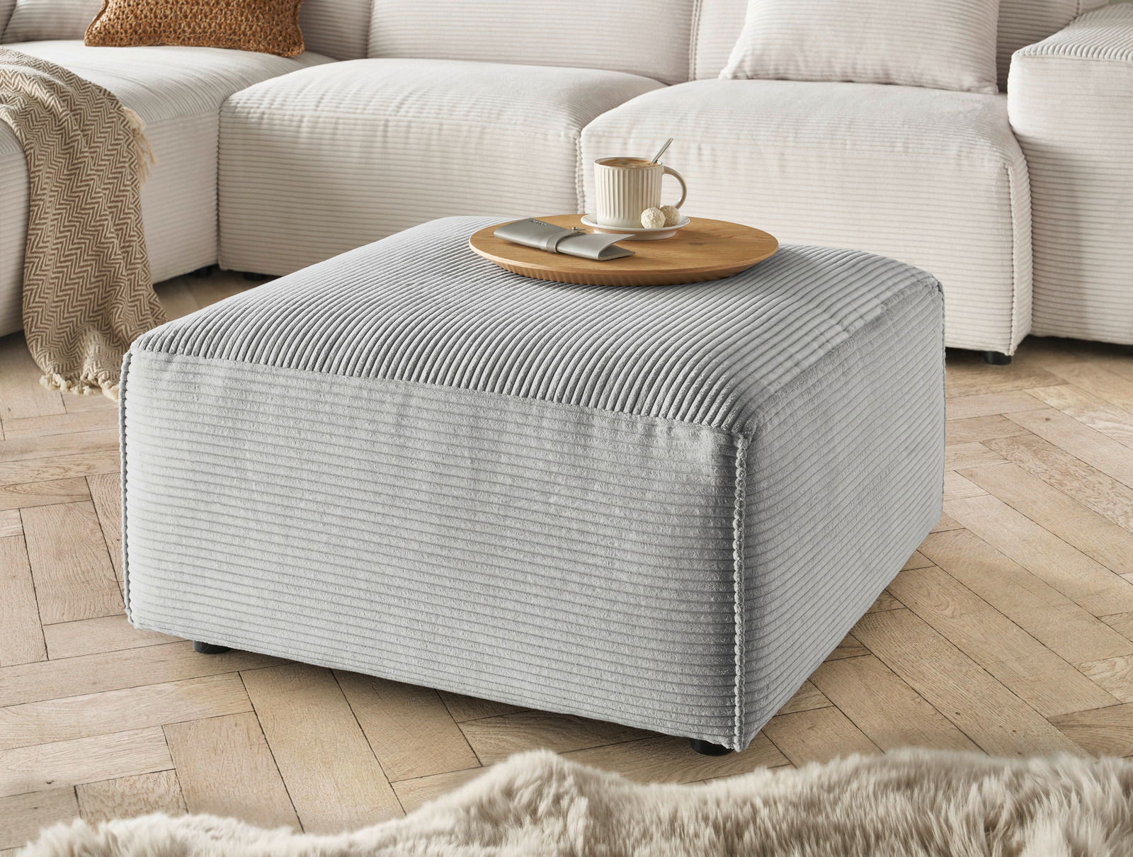 Lounge Handmade Hocker LH-EDINA Grauer Hocker aus Cordstoff in einer gemütlichen Wohnzimmerumgebung, seitliche Perspektive.