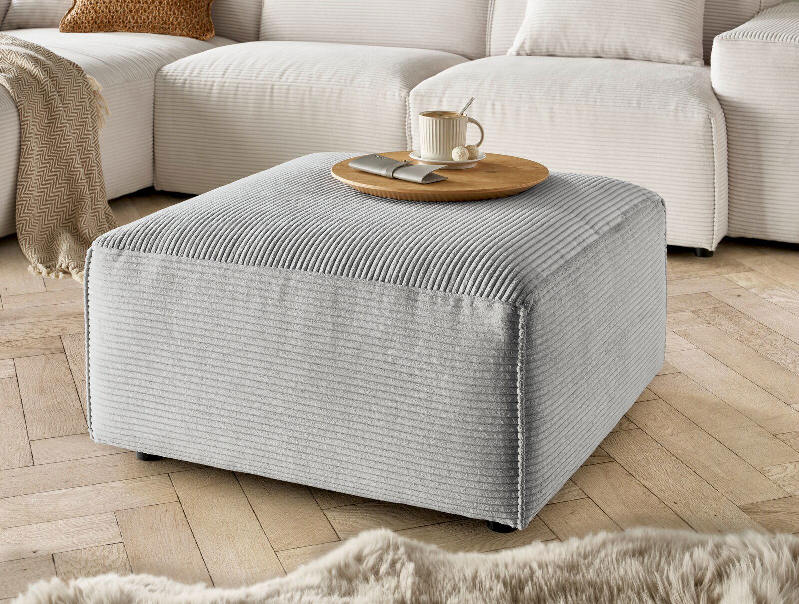 Lounge Handmade Hocker LH-EDINA Grauer Hocker aus Cordstoff in einer gemütlichen Wohnzimmerumgebung, seitliche Perspektive.