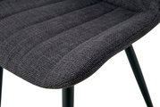 Detailaufnahme der gepolsterten Sitzfläche eines Stuhls mit dunkelgrauem Stoffbezug und schwarzen Metallbeinen, Perspektive schräg von oben
