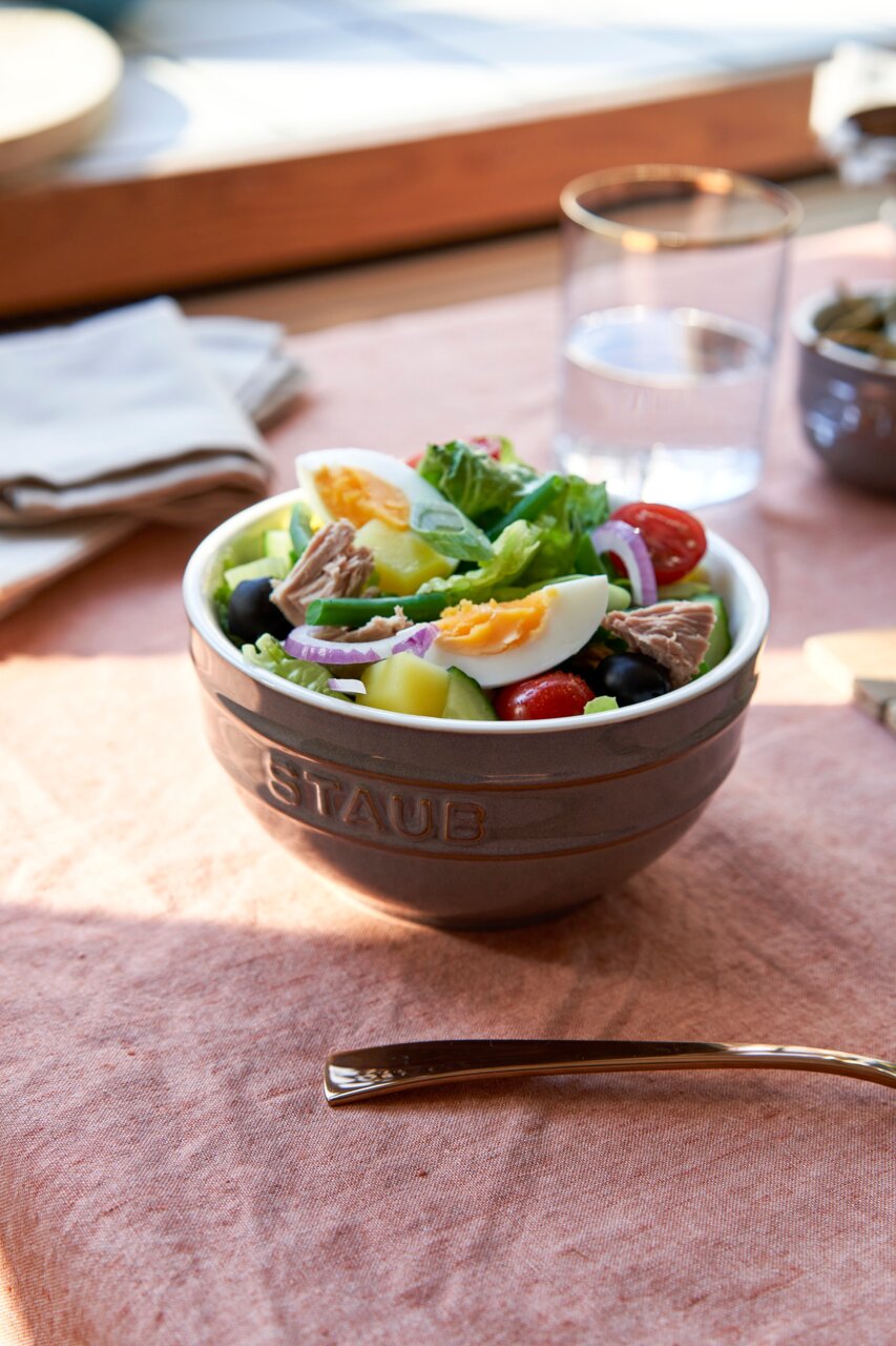 Een met stof bedekte grijze schaal, gevuld met een verse salade, gefotografeerd vanuit een zijaanzicht.