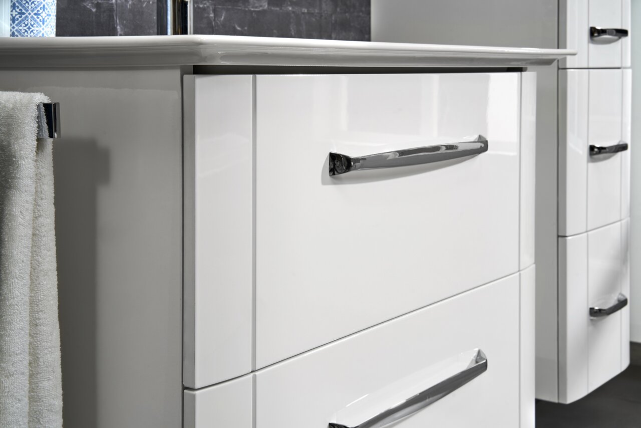 Nahaufnahme eines weißen Waschtischunterschranks mit glänzenden Chromgriffen, seitliche Perspektive