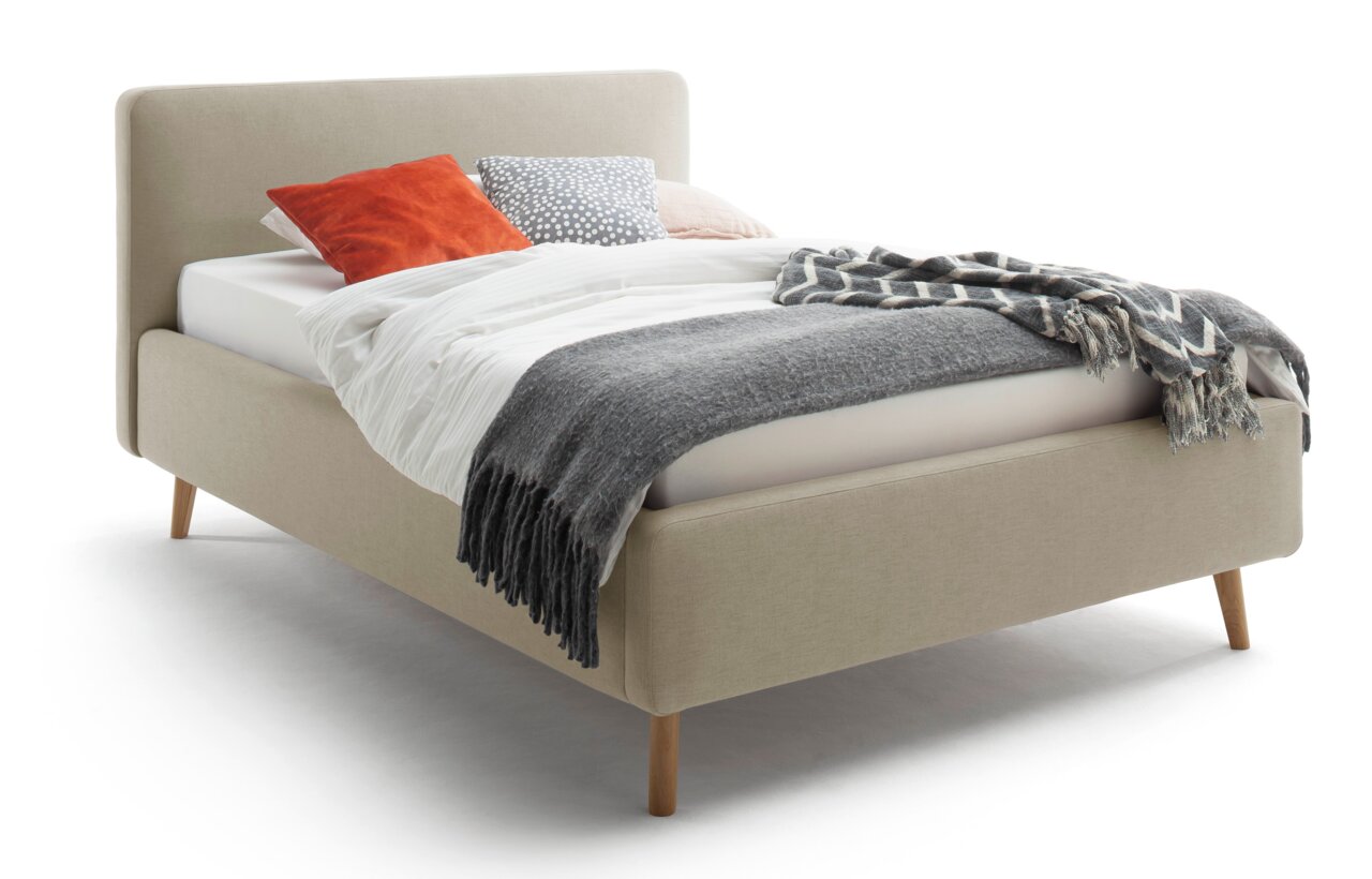 Z2 Polsterbett MATTIS Polsterbett MATTIS in Beige mit Holzfüßen, seitliche Perspektive, dekoriert mit Kissen und Decken.