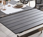 Moderner Ausziehtisch mit dunkler Tischplatte und Metallrahmen, gedeckt mit Geschirr und Gläsern, seitliche Perspektive.