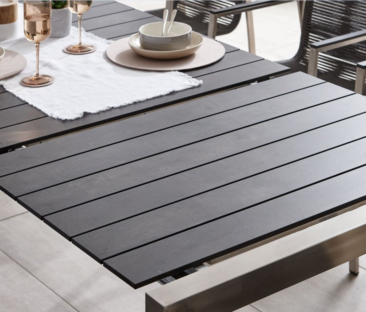 Moderner Ausziehtisch mit dunkler Tischplatte und Metallrahmen, gedeckt mit Geschirr und Gläsern, seitliche Perspektive.