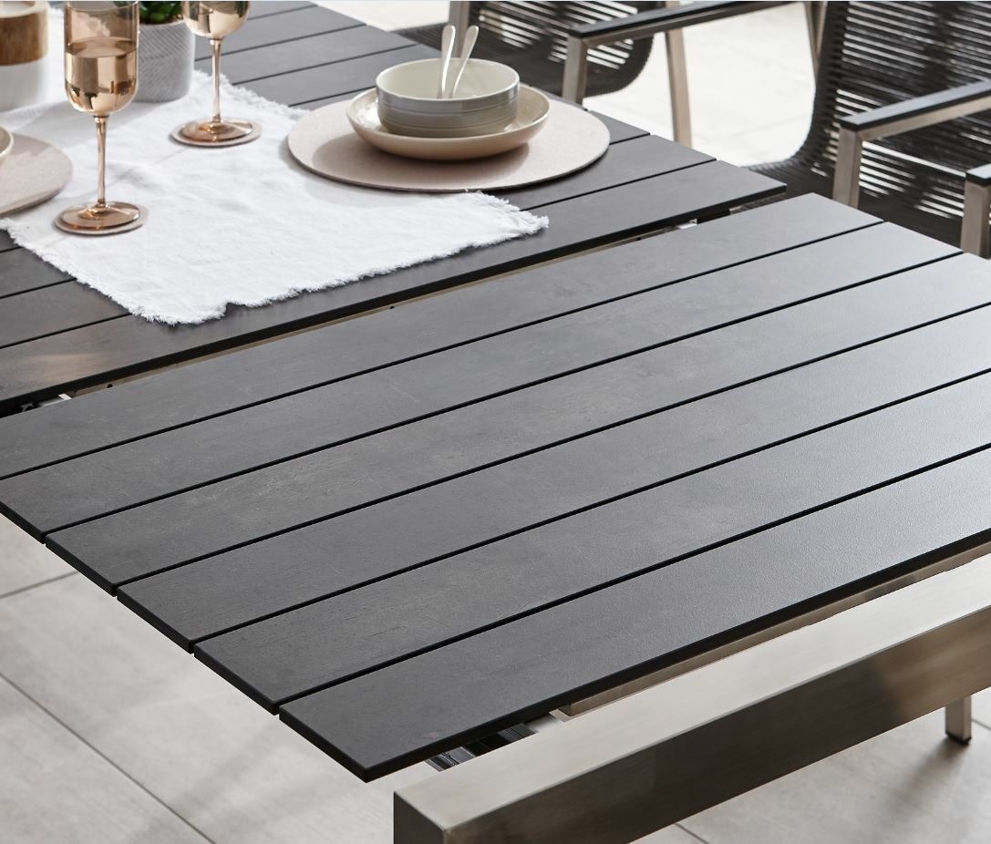 Moderner Ausziehtisch mit dunkler Tischplatte und Metallrahmen, gedeckt mit Geschirr und Gläsern, seitliche Perspektive.