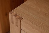 Nahaufnahme einer Ecke eines Sideboards aus hellem Holz mit sichtbaren Holzverbindungen, Perspektive von oben.