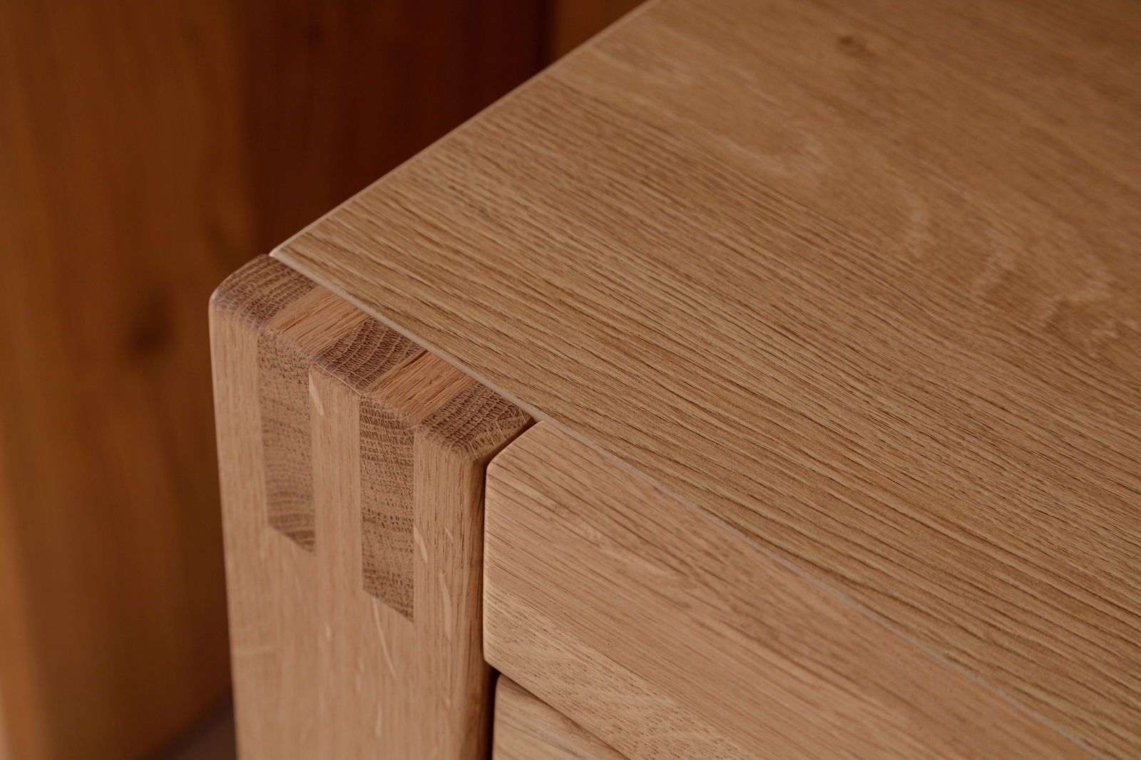 Nahaufnahme einer Ecke eines Sideboards aus hellem Holz mit sichtbaren Holzverbindungen, Perspektive von oben.