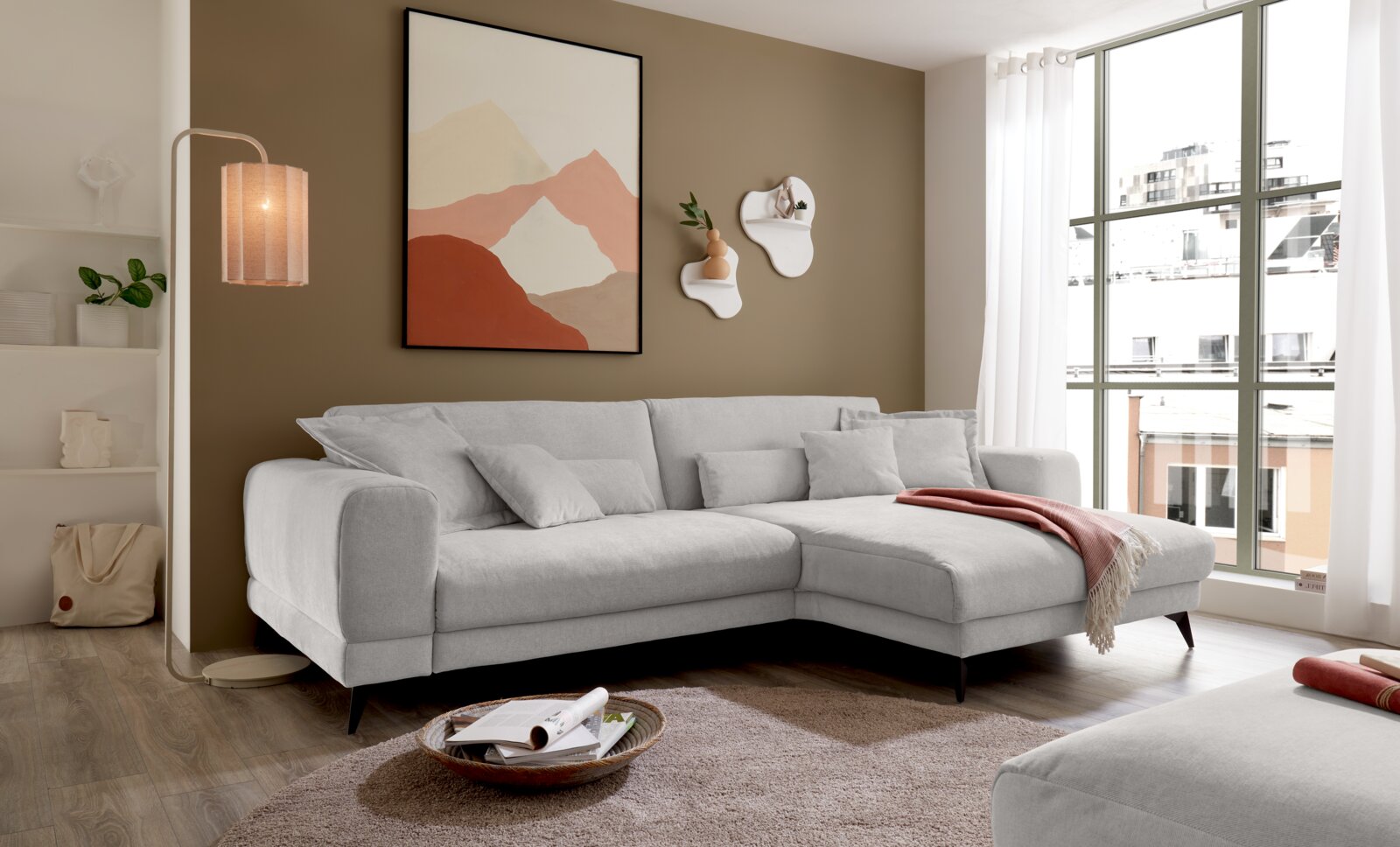 Set one by Musterring Hoekbank SET ONE MIDLAND Modernes hellgraues Ecksofa mit rechter Recamiere und schwarzen Füßen im Wohnzimmer, schräg von vorne aus leicht erhöhter Perspektive aufgenommen, neben großer Fensterfront und Stehlampe