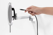 Seitliche Nahaufnahme eines runden, verchromten LED-Wandspiegels/Schminkspiegels mit ausziehbarem Schwenkarm, während eine Hand ein USB-C-Ladekabel zum Anschluss hält.