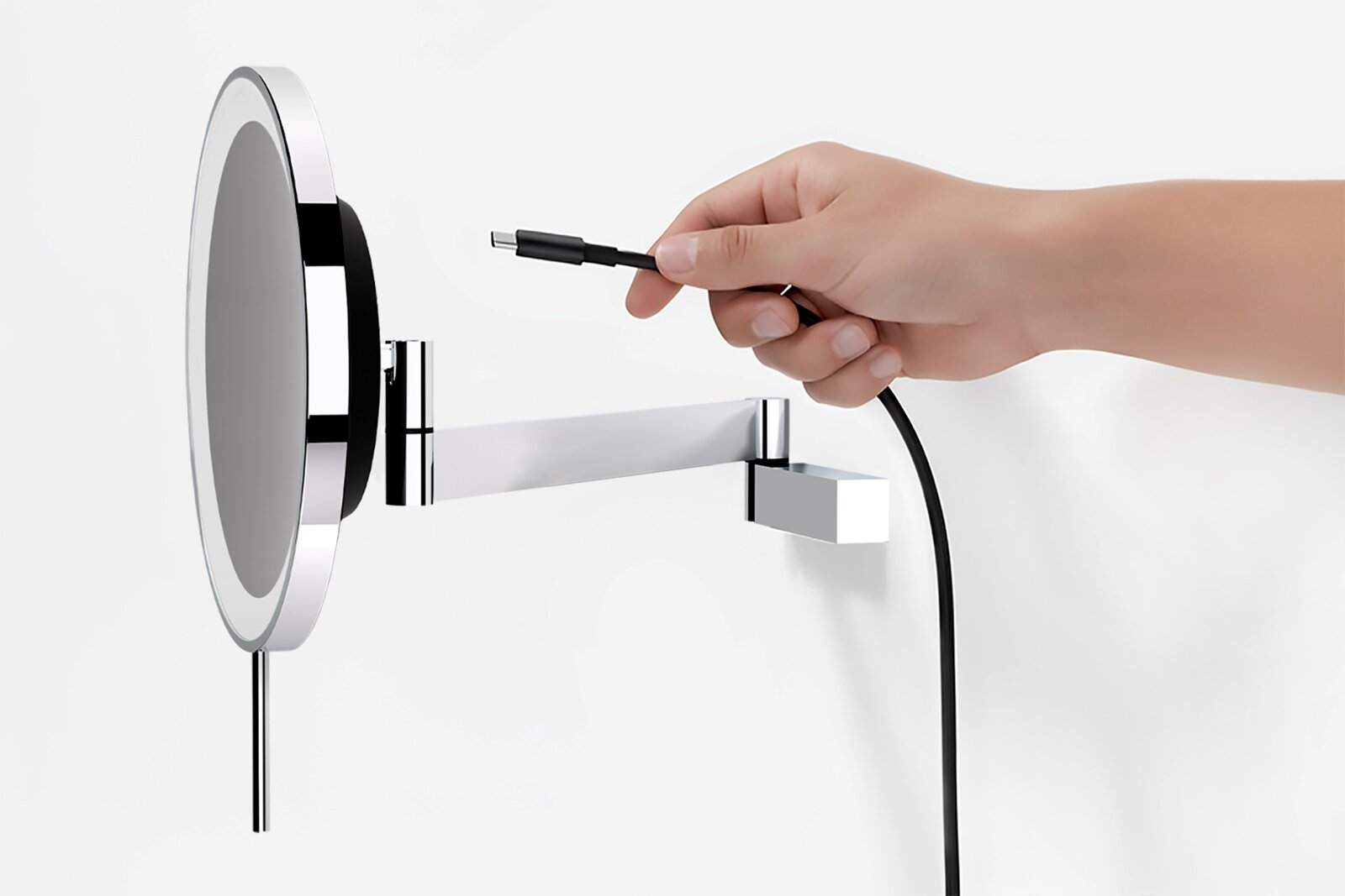 Seitliche Nahaufnahme eines runden, verchromten LED-Wandspiegels/Schminkspiegels mit ausziehbarem Schwenkarm, während eine Hand ein USB-C-Ladekabel zum Anschluss hält.