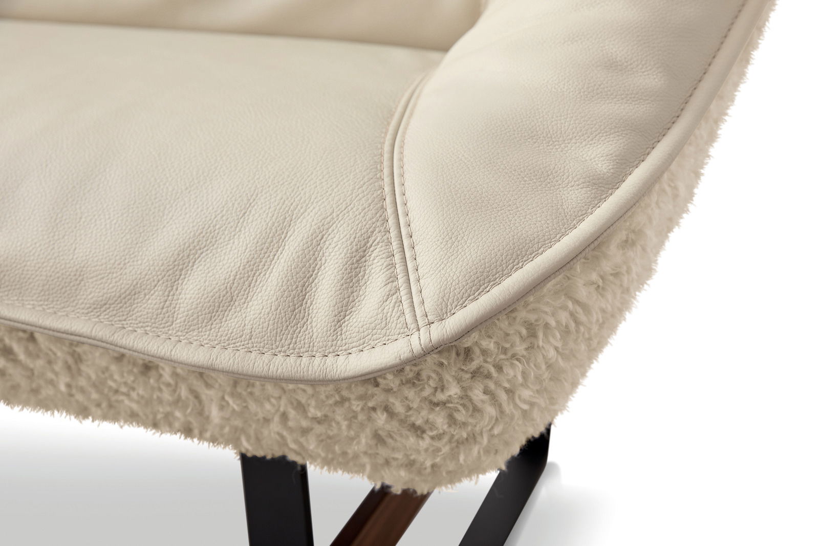 Nahaufnahme einer cremefarbenen Ledersitzfläche mit weicher, flauschiger Unterseite und schwarzen Metallbeinen, seitliche Perspektive.