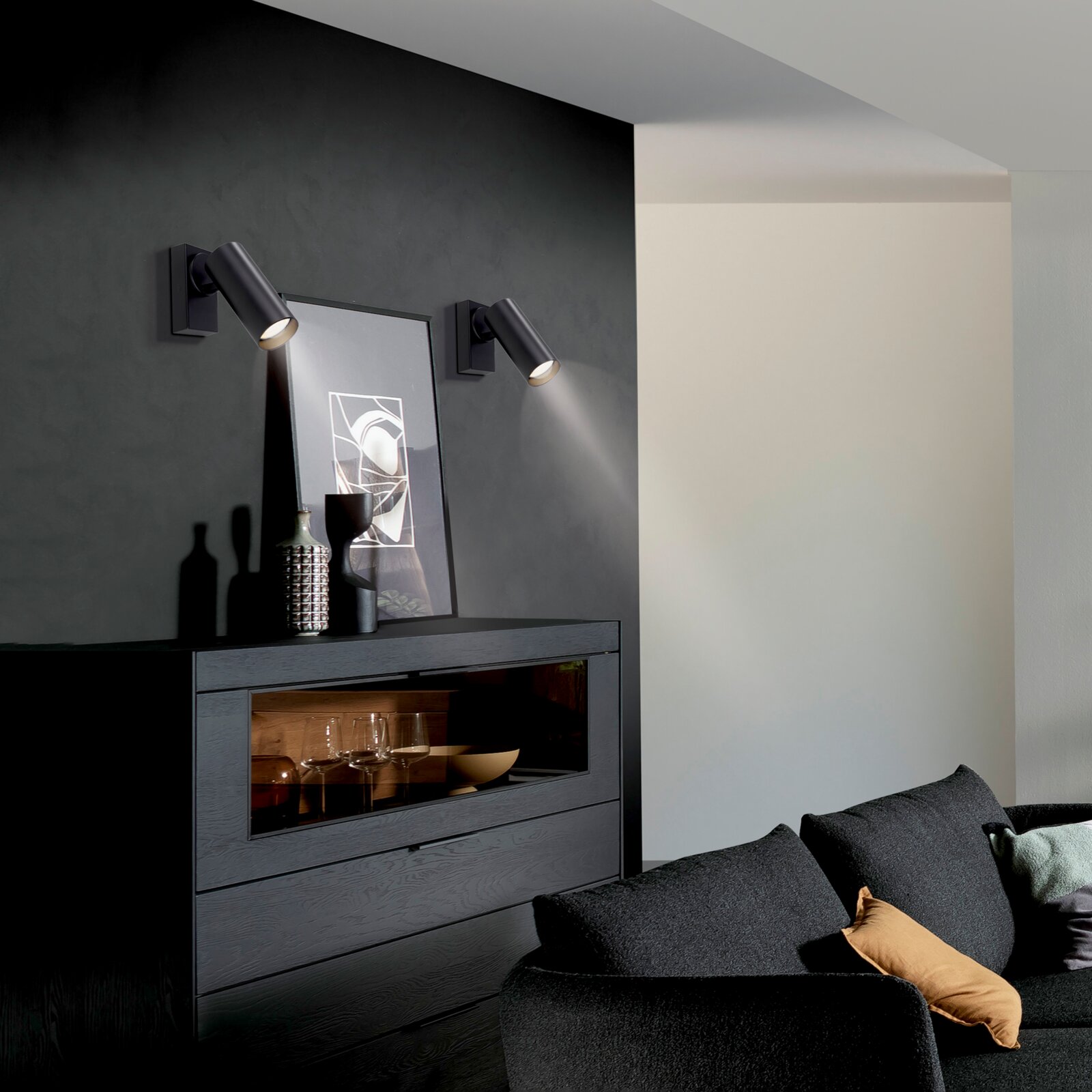 Moderne schwarze Wand-Spotleuchten als Paar über einem Sideboard an dunkler Akzentwand, Innenraumaufnahme in leichter Schrägansicht von vorn links