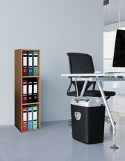 Schwarzer Aktenvernichter unter einem weißen Büroschreibtisch neben einem Holzregal mit farbigen Ordnern, aufgenommen aus seitlicher Perspektive auf Augenhöhe.
