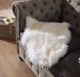 Weißes Lammfell Patchwork ca. 45x65cm auf einem braunen Sofa, von oben fotografiert.