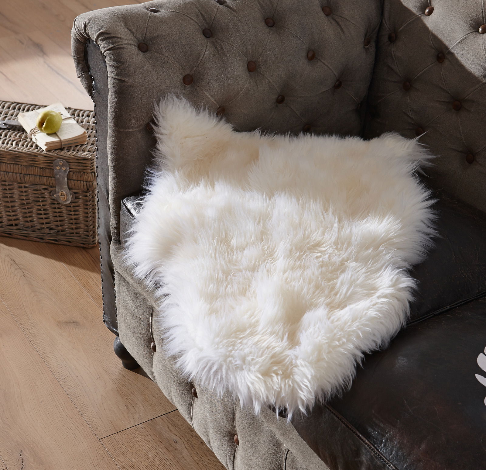 Weißes Lammfell Patchwork ca. 45x65cm auf einem braunen Sofa, von oben fotografiert.