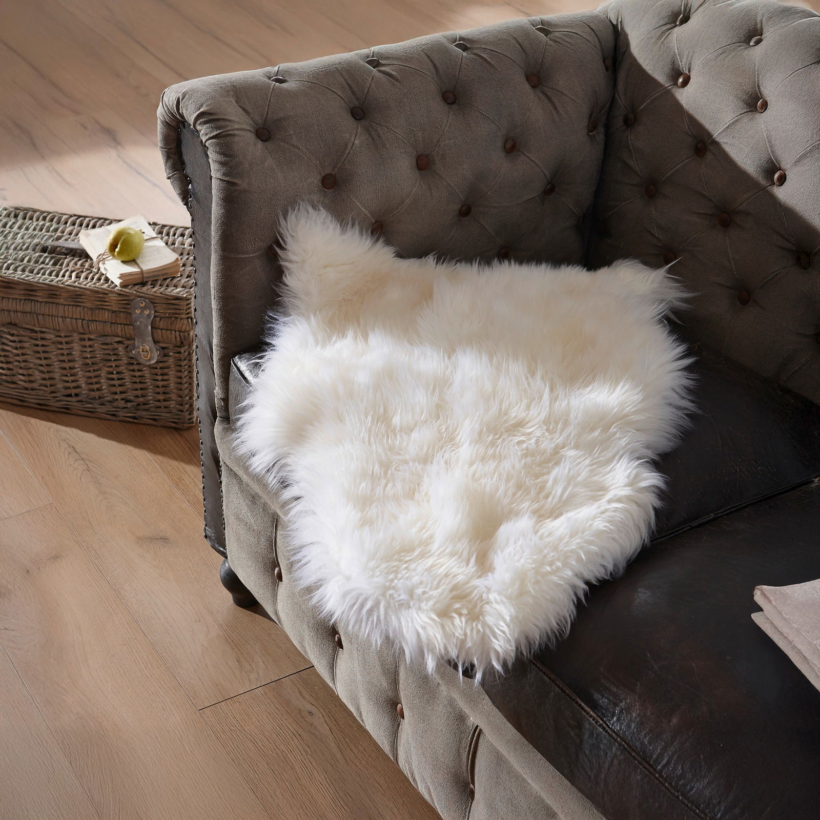 Weißes Lammfell Patchwork ca. 45x65cm auf einem braunen Sofa, von oben fotografiert.