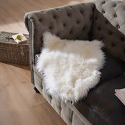 Weißes Lammfell Patchwork ca. 45x65cm auf einem braunen Sofa, von oben fotografiert.