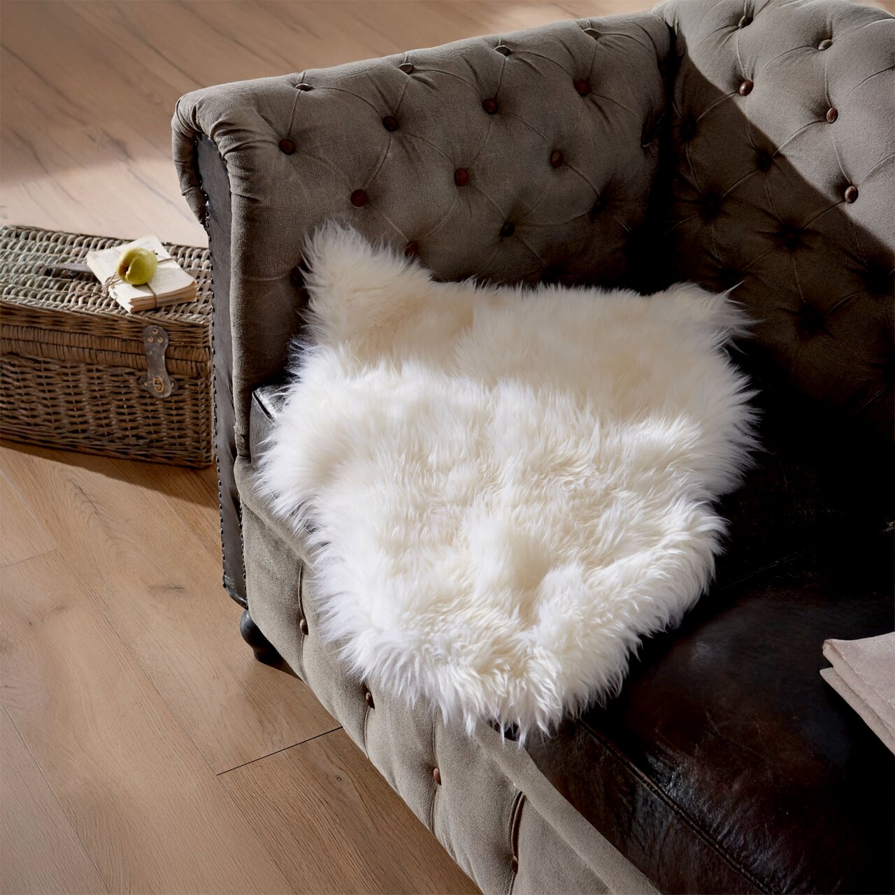 Weißes Lammfell Patchwork ca. 45x65cm auf einem braunen Sofa, von oben fotografiert.