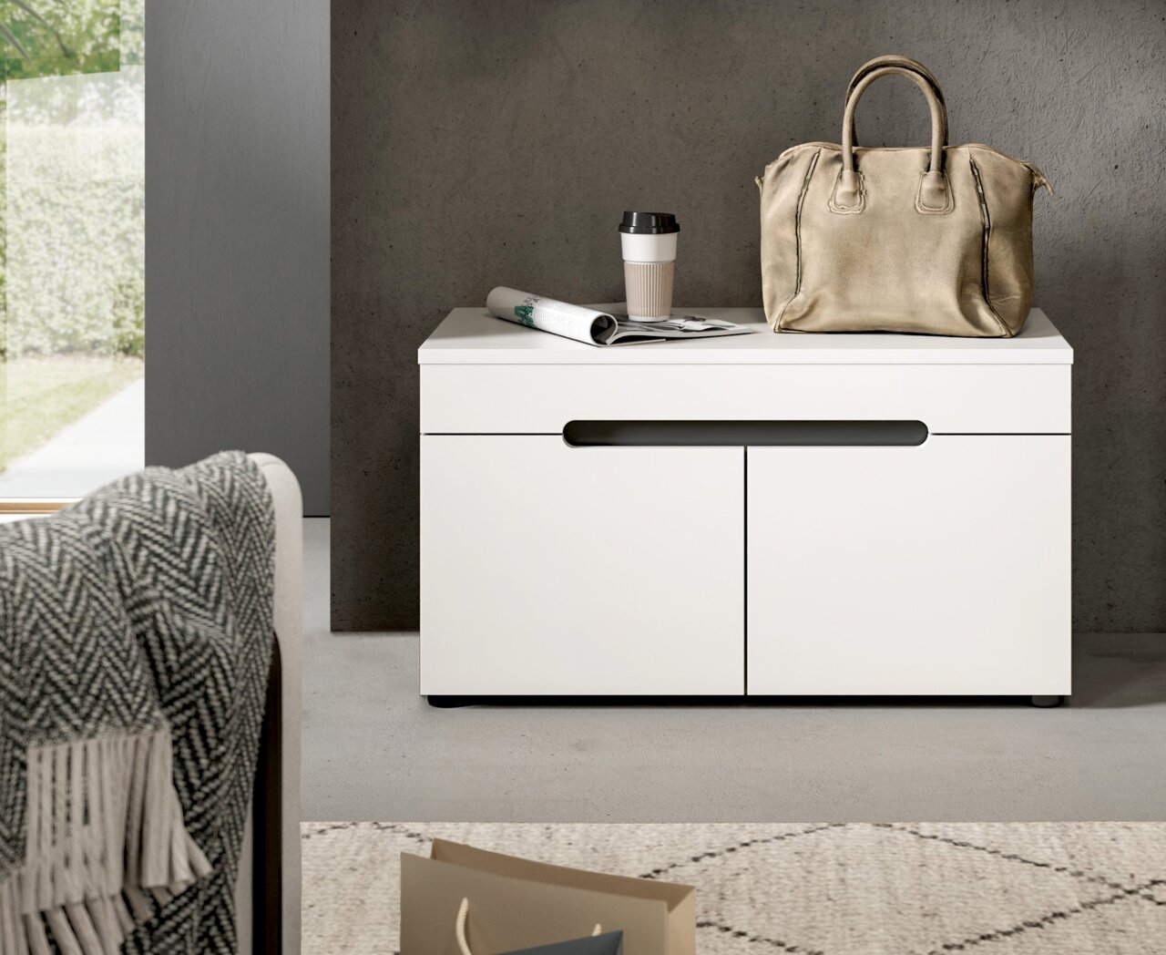 Weiße, moderne Kommode mit zwei Türen und schwarzer Griffleiste, darauf Handtasche, Kaffeebecher und Zeitung; frontale Perspektive auf das Möbelstück.