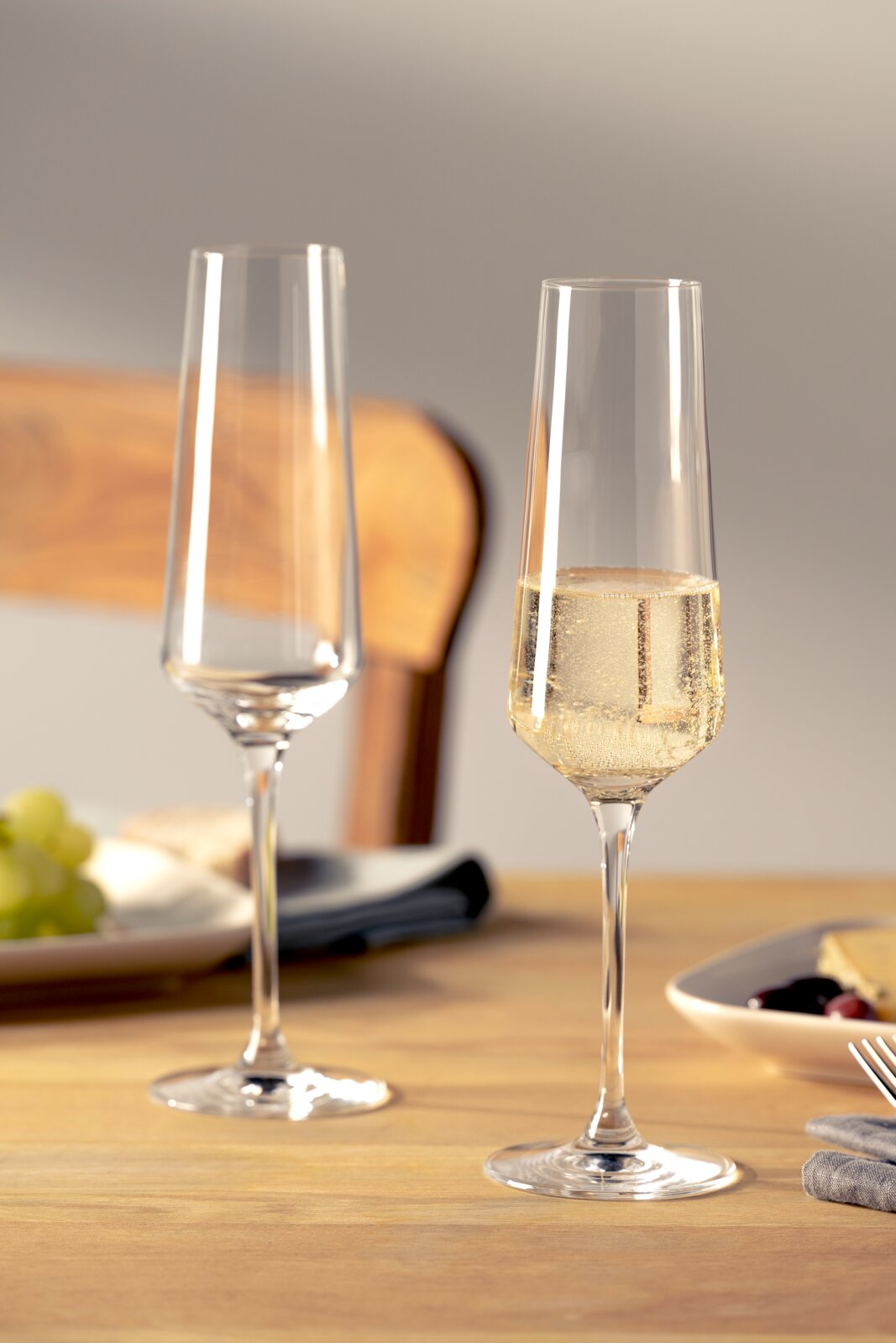 Leonardo Set van 6 champagneglazen PUCCINI Twee elegante champagneglazen op een gedekte tafel, waarvan één gevuld met bruisende champagne, gefotografeerd vanuit een zijdelingse hoek.