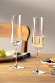 Zwei elegante Sektgläser auf einem gedeckten Tisch, eines gefüllt mit sprudelndem Sekt, aus seitlicher Perspektive fotografiert.