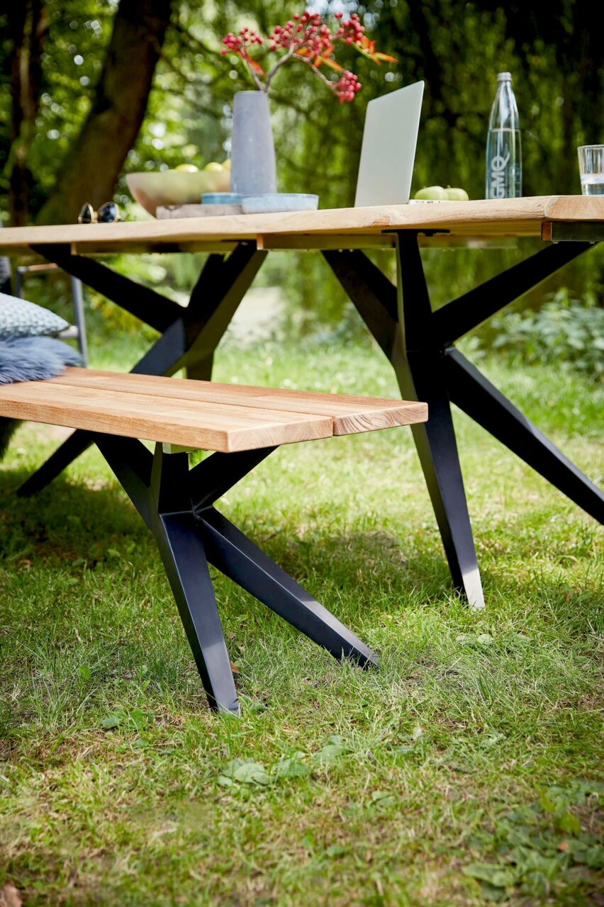 Holzbank mit schwarzem Metallgestell im Garten, seitliche Perspektive