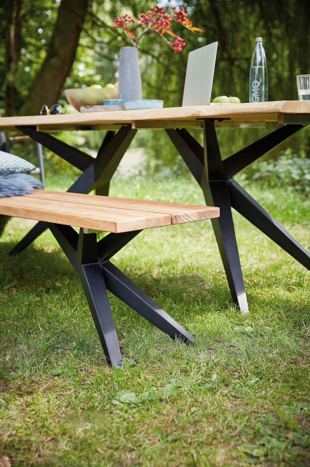 Holzbank mit schwarzem Metallgestell im Garten, seitliche Perspektive