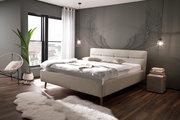 Modernes Polsterbett in einem stilvollen Schlafzimmer mit großen Fenstern, dekorativen Flügeln an der Wand und gemütlicher Beleuchtung, seitliche Perspektive.