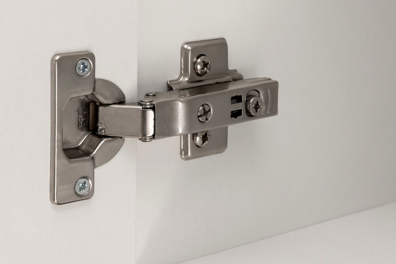 Nahaufnahme eines Metallscharniers an einer weißen Schranktür, seitliche Perspektive.