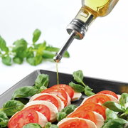 Nahaufnahme eines Ausgießers, der Öl auf einen frischen Tomaten-Mozzarella-Salat mit Basilikumblättern träufelt.