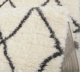 Nahaufnahme eines flauschigen, cremefarbenen Teppichs mit grauem Rautenmuster, teilweise aufgerollt.