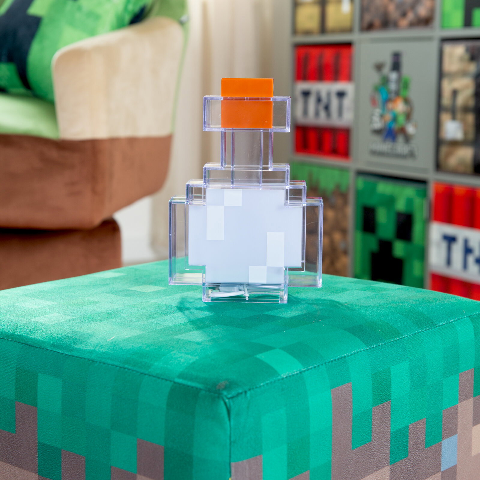 Transparente, pixelige LED-Lampe in Flaschenform mit orangefarbenem Deckel auf grünem, Minecraft-inspiriertem Hocker, frontal aus leicht erhöhter Perspektive fotografiert.