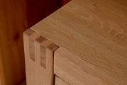 Detailansicht einer Ecke eines Highboards aus Holz mit sichtbarer Maserung und präziser Verarbeitung.