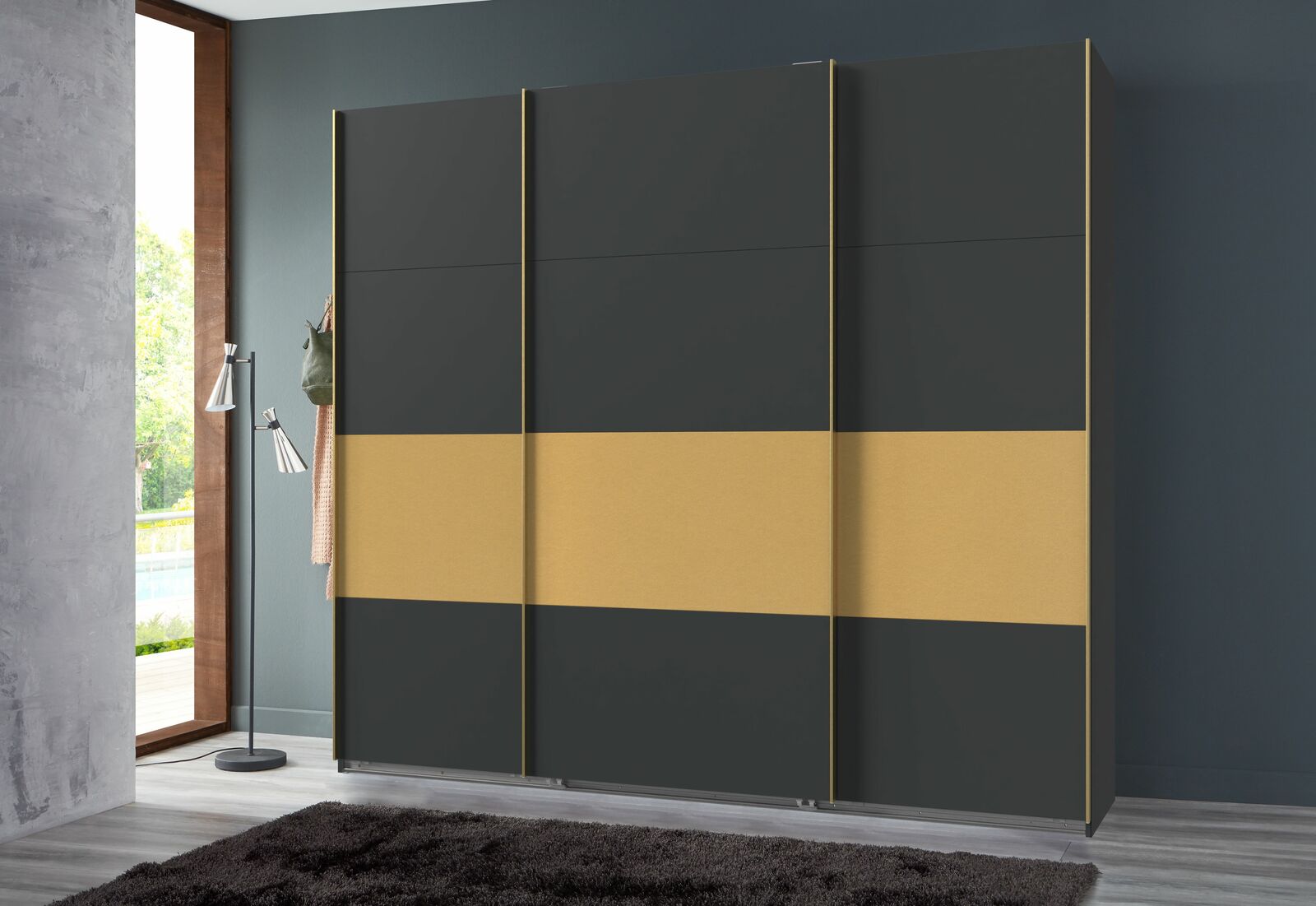 Moderner dreitüriger Schwebetürenschrank in dunklem Grau mit breitem goldenen Streifen, frontal abgebildet in einem stilvollen Raum.