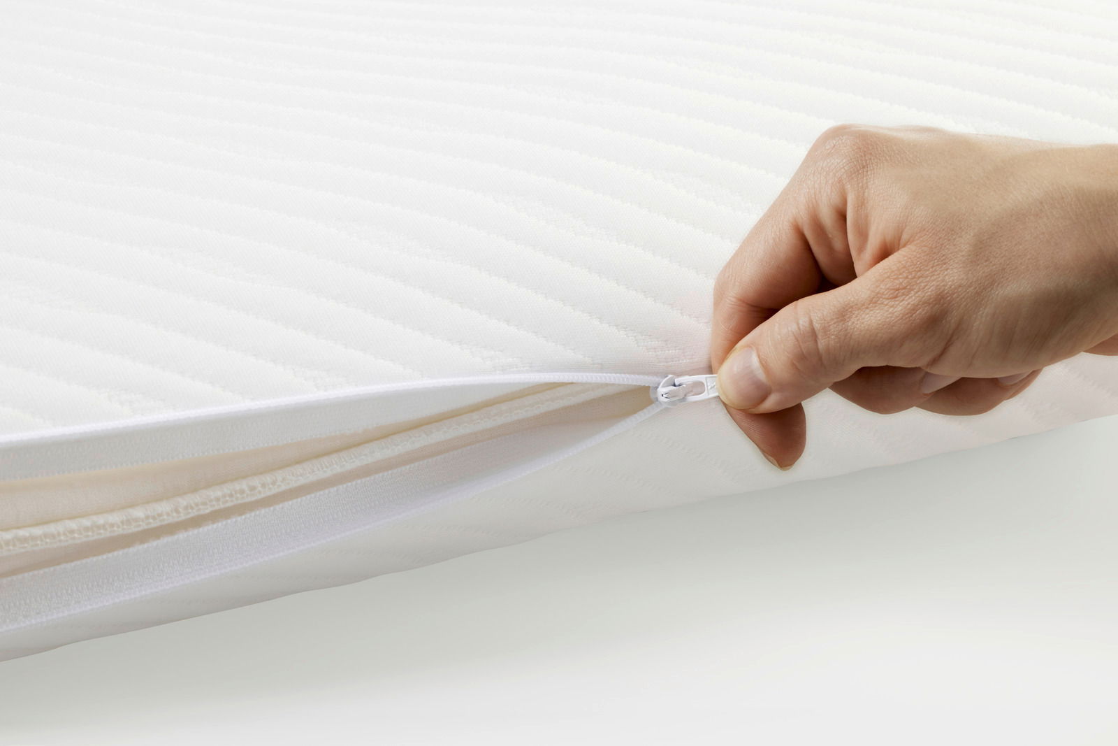 Nahaufnahme eines weißen Schlafkissens mit Reißverschluss, der von einer Hand geöffnet wird.