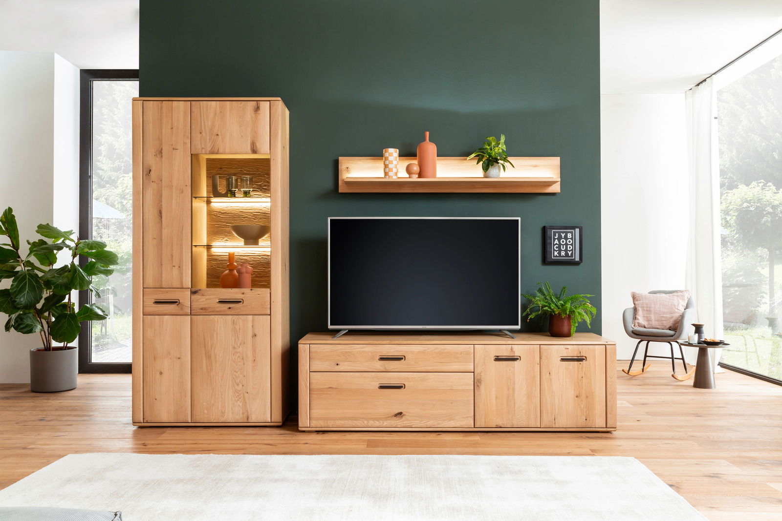 Moderne Wandkombination aus Holz in einem Wohnzimmer, bestehend aus einem hohen Schrank mit Glaseinsatz, einem TV-Board und einem Wandregal. Perspektive: Frontalansicht.
