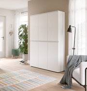 Weißer, moderner Mehrzweckschrank mit vier grifflosen Türen in einem hellen Wohnraum, fotografiert in leichter Schrägansicht von vorn