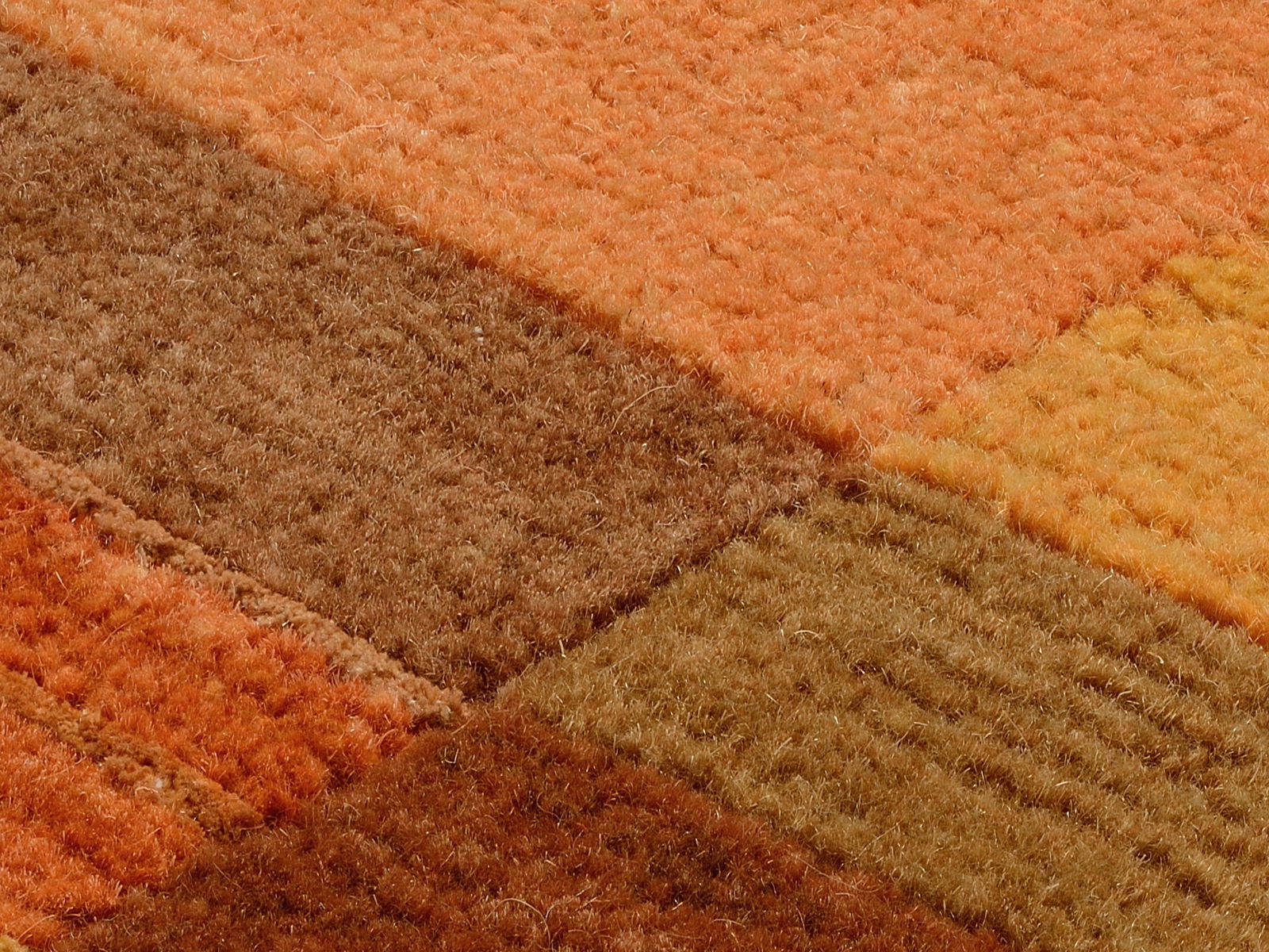 Nahaufnahme eines Teppichs mit quadratischem Muster in warmen Erdtönen wie Orange, Braun und Gelb, aus einer schrägen Perspektive fotografiert.