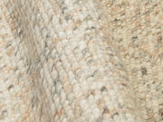 Nahaufnahme eines handgewebten Teppichs mit grober Textur in natürlichen Farbtönen, seitliche Perspektive.