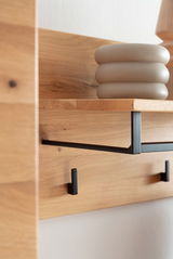 Nahaufnahme eines Garderobenpaneels aus Holz mit schwarzem Metallhaken und Ablage, seitliche Perspektive.