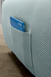 Nahaufnahme einer strukturierten, hellblauen Sofaecke mit integrierter Tasche, die ein blaues Buch enthält, auf einem Holzboden.