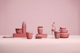 Eine stilvolle rosa Trinkflasche mit 700 ml Fassungsvermögen, umgeben von passenden Küchenutensilien, aus seitlicher Perspektive fotografiert.
