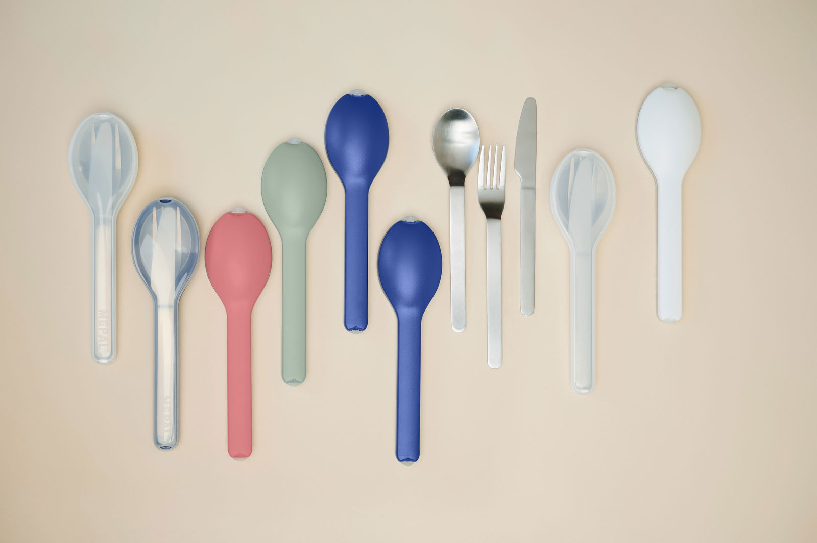 Mepal Besteck-Set 3-tlg. Nordic sage ELLIPSE Verschiedene Bestecksets in bunten Hüllen, darunter Löffel, Gabel und Messer, aus der Vogelperspektive auf einem beigen Hintergrund.