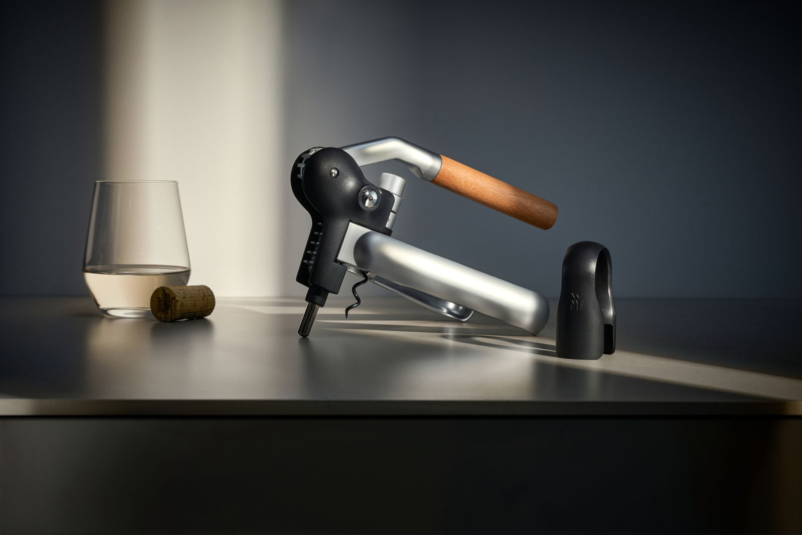 WMF Hebelkorkenzieher Seitliche Ansicht eines WMF Baric Hebelkorkenziehers mit Holzgriff, neben einem Glas und einem Korken auf einem Tisch.