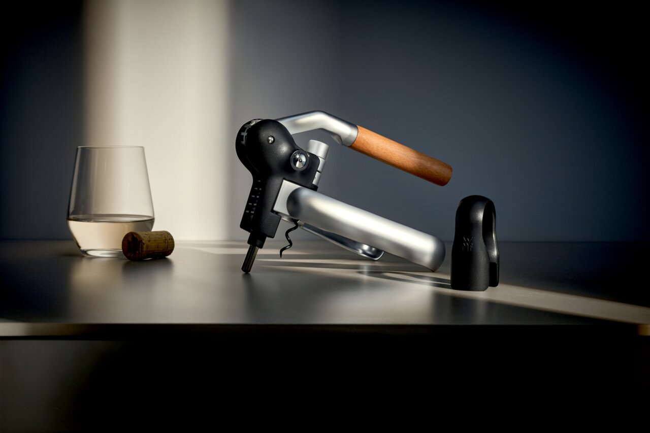 WMF Hebelkorkenzieher Seitliche Ansicht eines WMF Baric Hebelkorkenziehers mit Holzgriff, neben einem Glas und einem Korken auf einem Tisch.