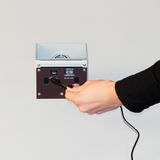 Vorderansicht einer silbernen AKKU-Wandleuchte mit USB-Anschluss und Schalter für On, Off und Auto, während eine Hand ein Kabel einsteckt.