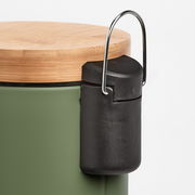 Nahaufnahme eines grünen Kosmetikeimers mit einem Deckel aus Holz und einem schwarzen Kunststoffelement an der Seite, seitliche Perspektive.